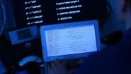 Ein Mann sitzt vor einem Rechner mit Computer Quellcode auf dem Bildschirm.  (picture alliance /dpa / Oliver Berg)